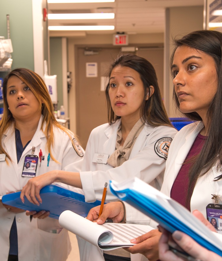 Mercer graduate students are pictured in white coats, holding clipboards.