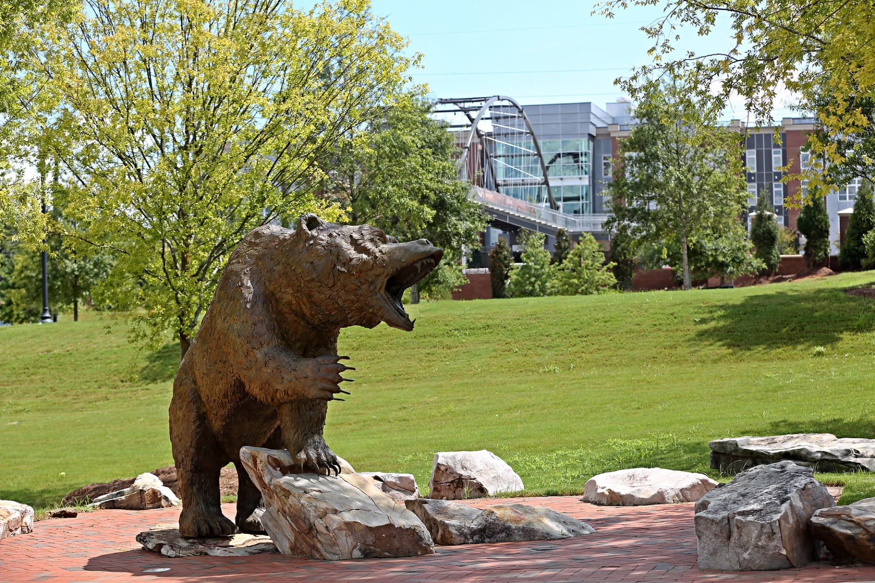 A bear statue is pictured, with the Lofts at Mercer Landing and pedestrian bridge in the background.