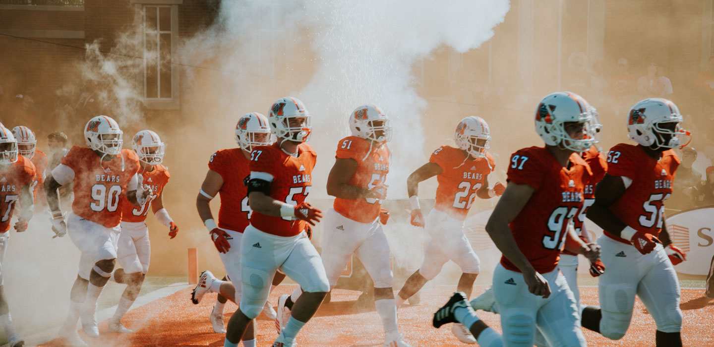 Football players rush the field in orange jerseys