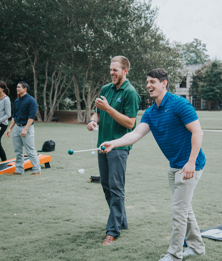 Graduate students smile while playing cornhole