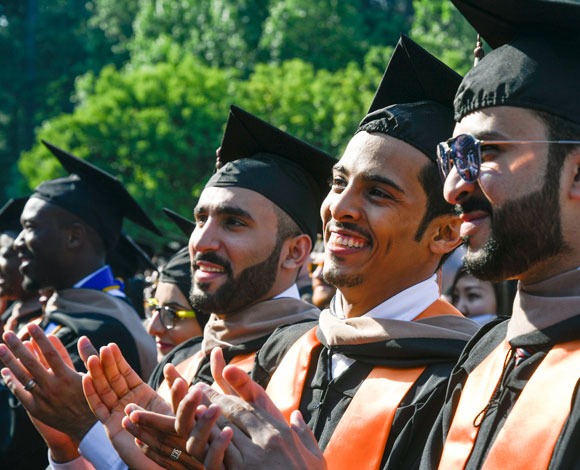 Three students smile at outdoor commencement ceremony