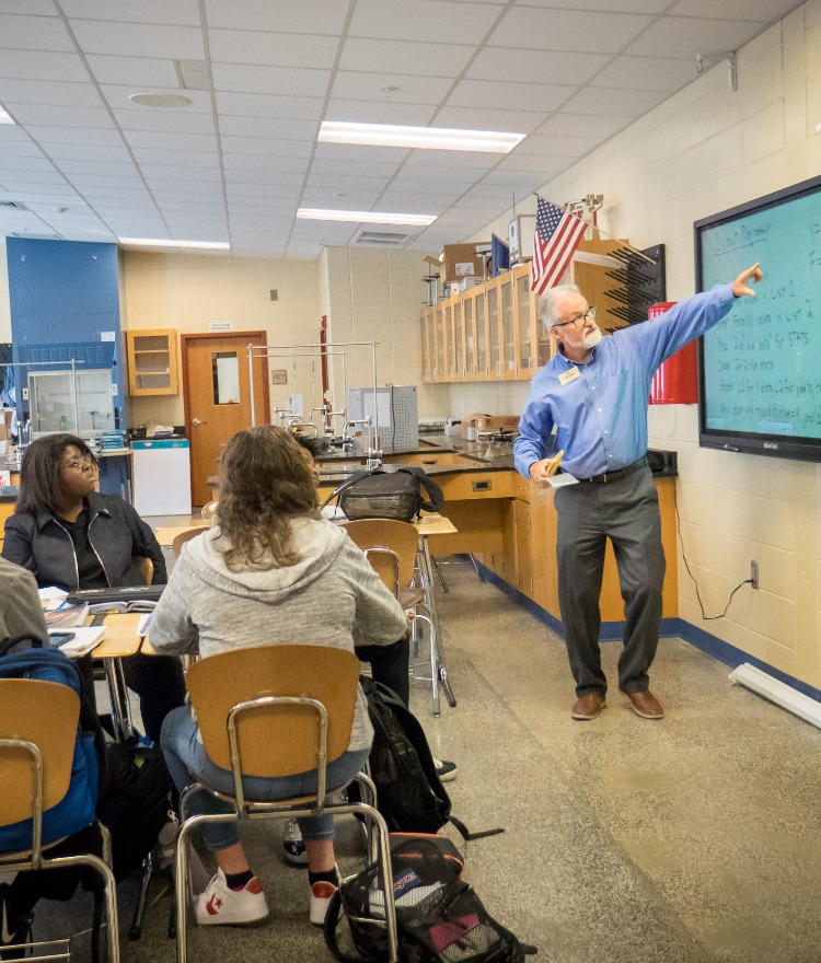A teacher points at the board in a high school physics class.