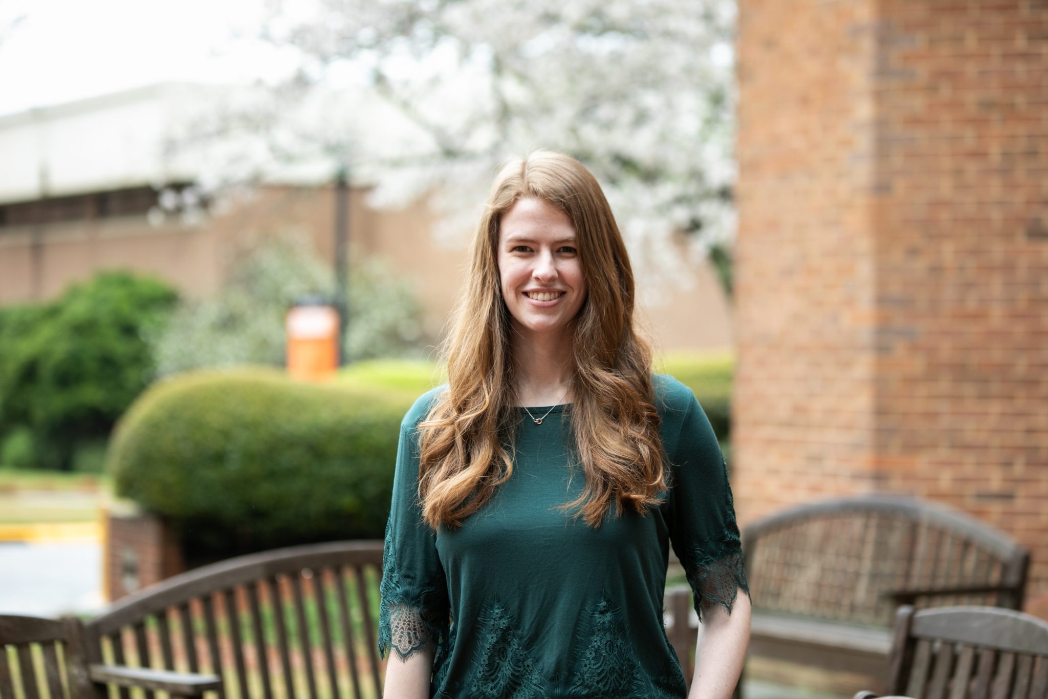 A young woman wearing a dark green shirt stands in front of a bench