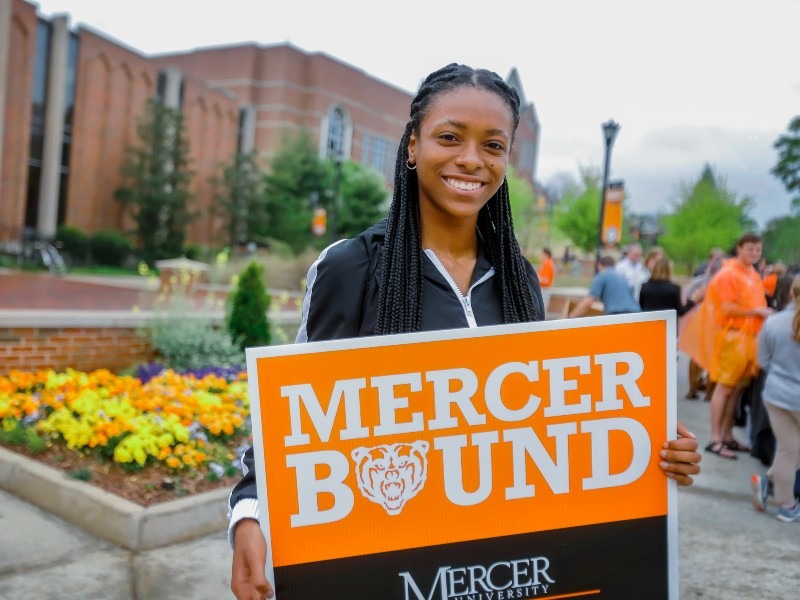 A young woman holds a sign that says Mercer Bound