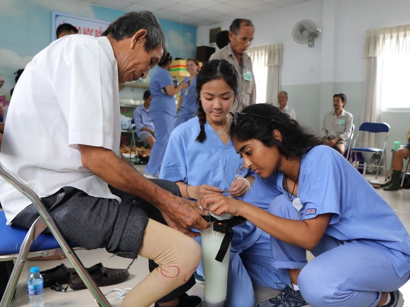 Two young women wearing scrubs fit a prosthetic leg on a man