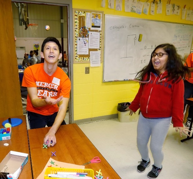 A young man wearing an orange Mercer shirt tosses the ball while a girl jumps up