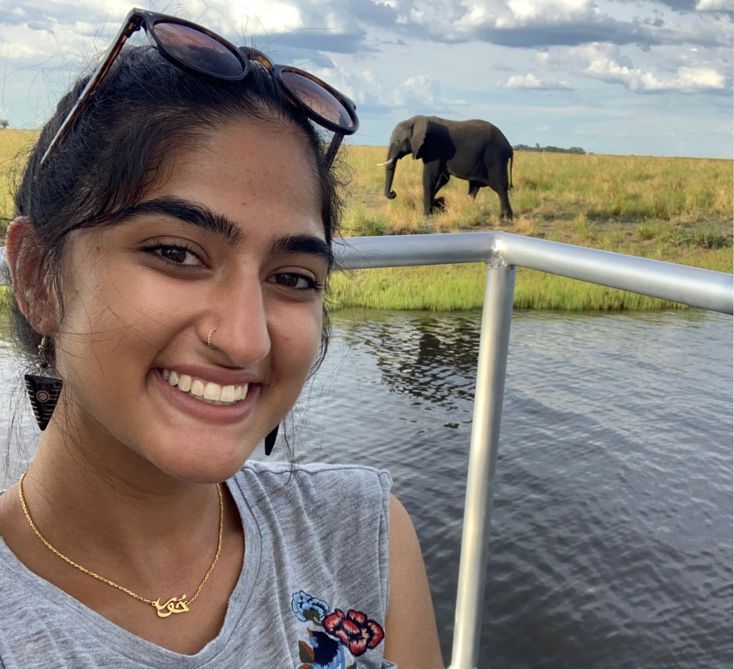 A young woman takes a selfie with an elephant in the background