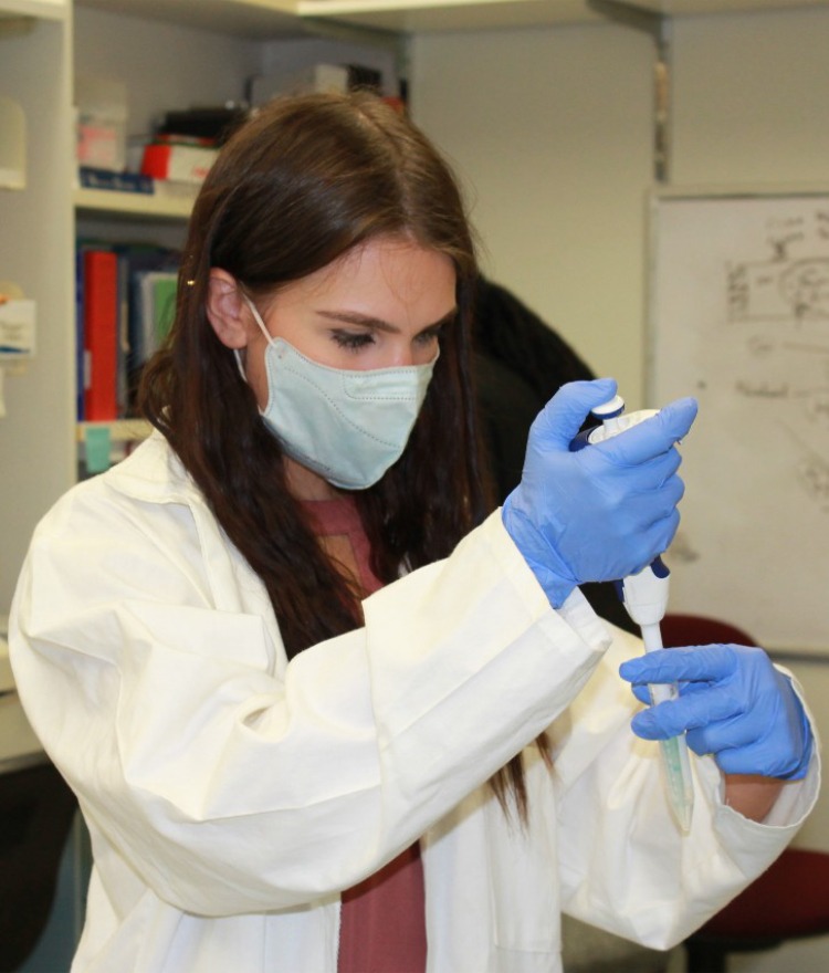 A Mercer student wearing a white lab coat and blue gloves works in a lab