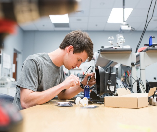 A male student works with robotics tools in a lab