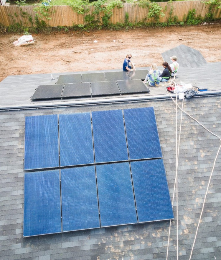 Four Mercer students wearing harnesses sit on a home's roof where they are installing solar panels