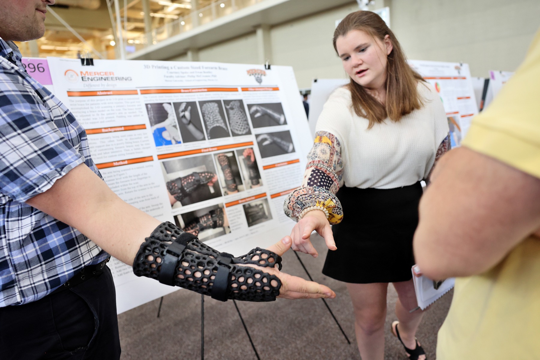 A woman points to a man's wrist which has a 3D printed brace on it