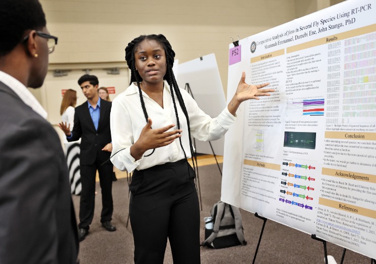 a college student gestures at a poster showing her research