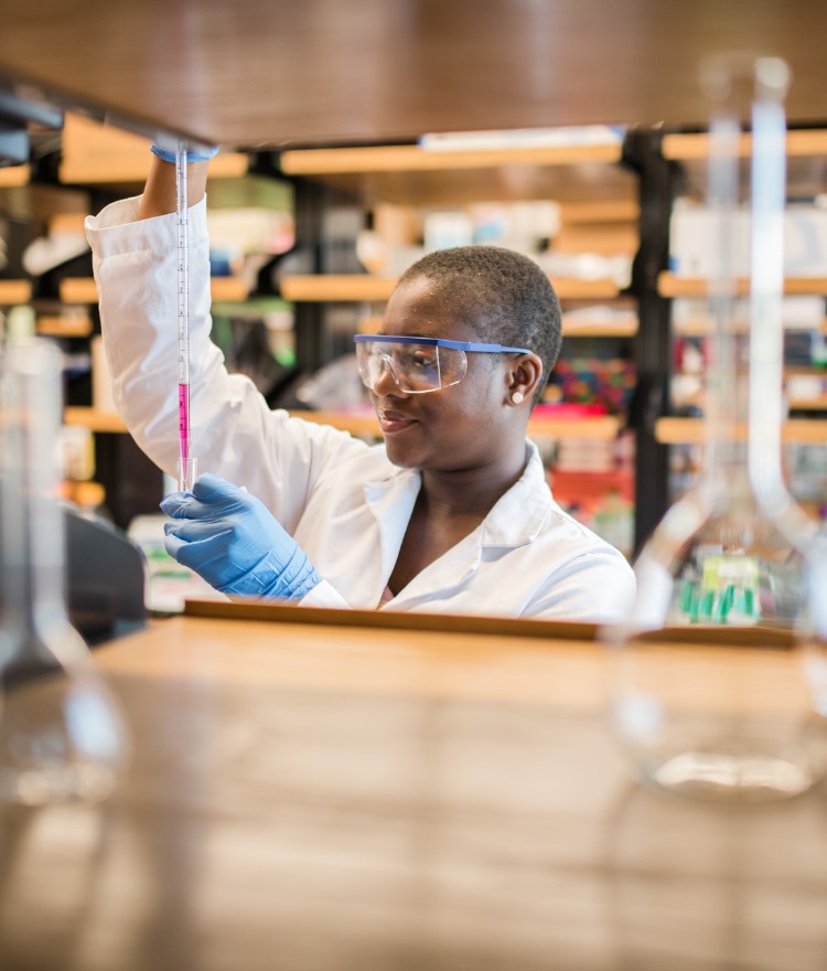 A college students looks at liquid in a pipette in a lab