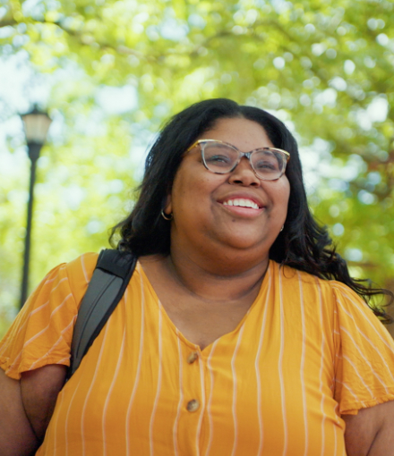 A young woman is wearing a yellow shirt in front of a background of trees