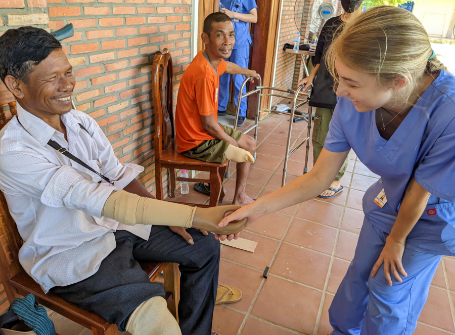 A female Mercer student wearing scrubs shakes the new prosthetic hand of a Cambodian man
