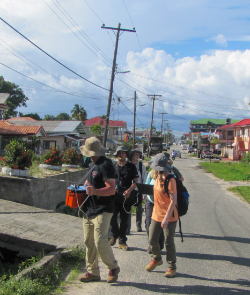 students walk down a street using a machine to check levels of mercury in the air