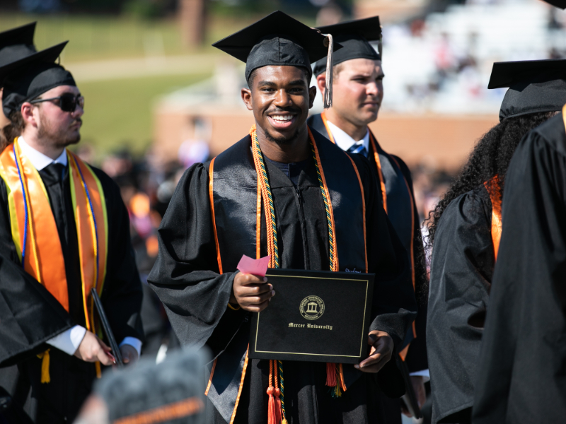 A recent graduate holds up his diploma
