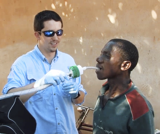 a man wearing sunglasses holds a tube connected to a host to another man's mouth