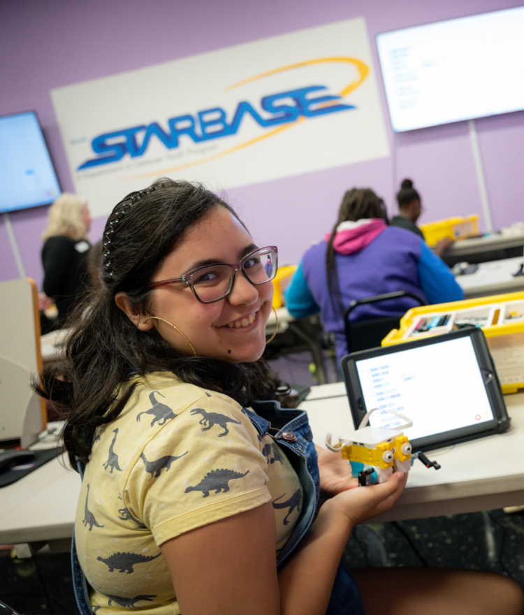 A middle school girl smiles while holding a robot made out of legos.