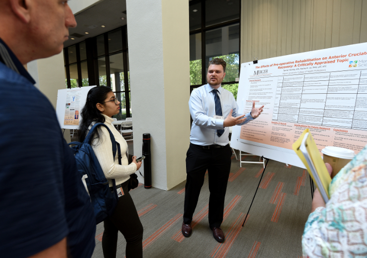 a male student gestures toward a poster while three people look on