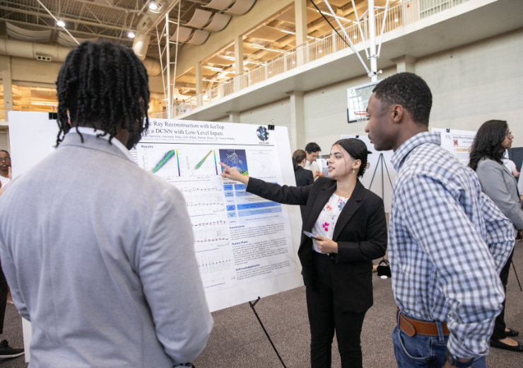 a female student points to a poster while two others look on