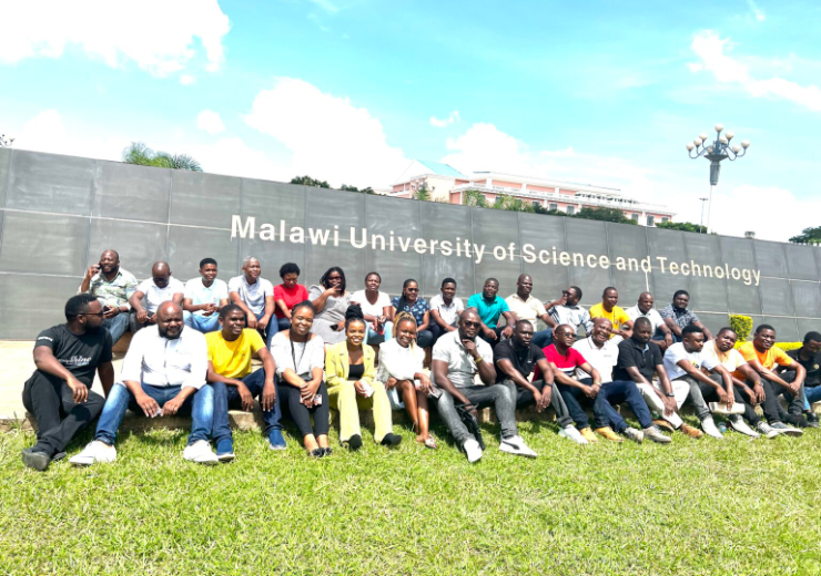 A group of people is shown in front of a sign for Malawi University of Science and Technology