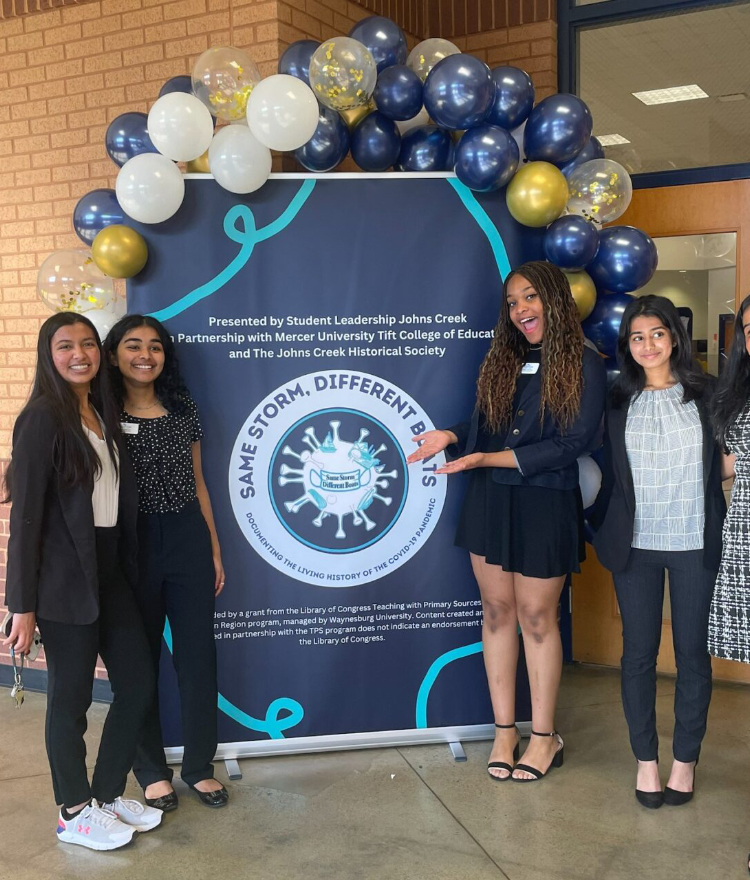 Five female students stand in front of a large poster with balloons