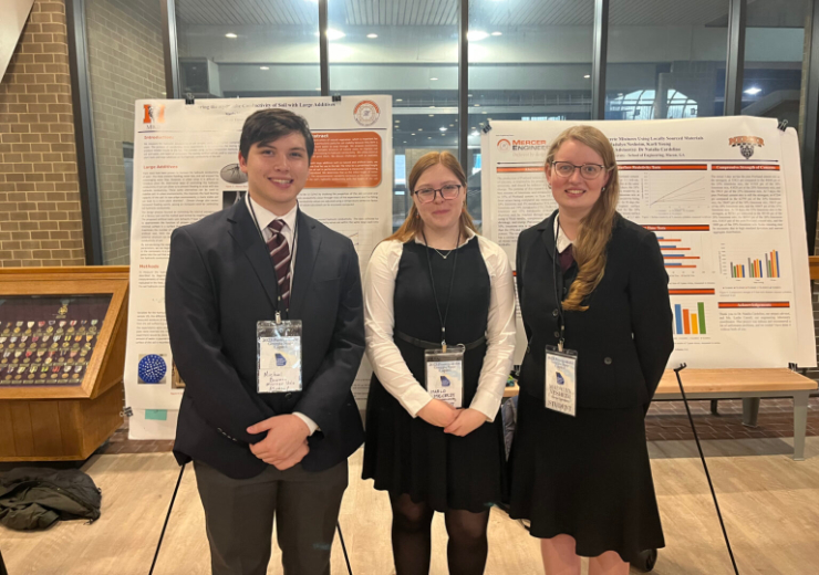 three students stand in front of two posters