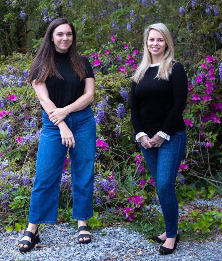 two women stand in front of a flowering bush
