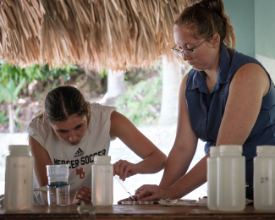 two women use a pipette to suck up a small amount of water from a petri dish