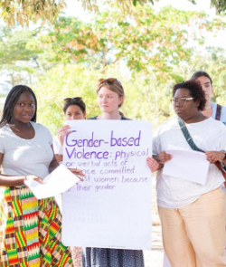 three women talk while the one in the middle holds on a poster that says