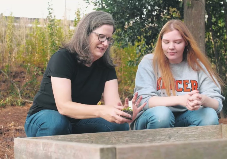 a professor and a student put a small plant in a bed