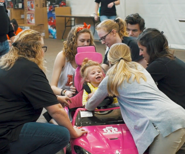 mercer students fit a toddler in a child-sized car