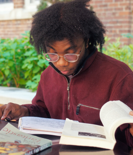 a young man sits at a table and reads a textbook