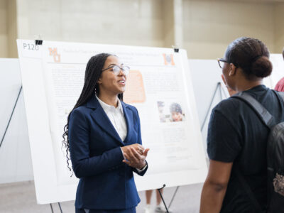 a woman wearing a suit stands in front of a poster and talked to another woman