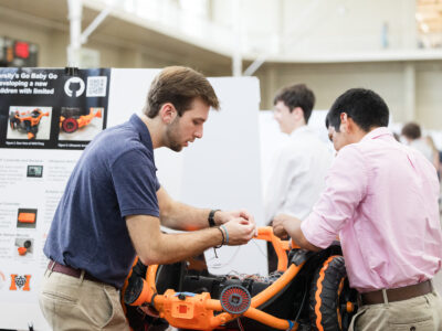 two men work on a mobility device with wheels