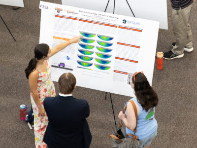 An aerial view of a Mercer University student presenting her poster, titled "Time-Dependent Solar and Sidereal Signal Maps," to two individuals during BEAR Day.