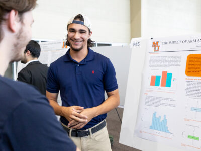 A Mercer University student stands next to his poster at BEAR Day.