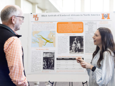 A Mercer University student presents her poster titled "Illicit Arrivals of Enslaved Africans to North America" to a faculty member at BEAR Day.