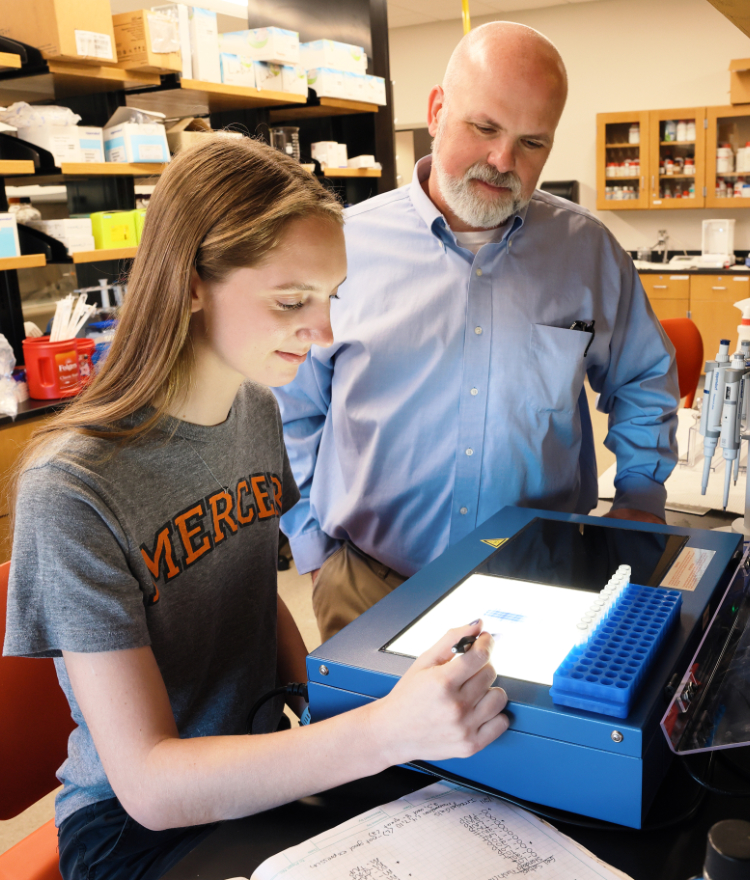 A Mercer undergraduate student uses scientific equipment, supervised by a professor, in a lab.