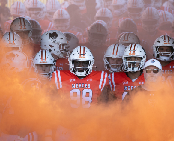 Mercer football players together amid orange smoke, preparing to enter the field.
