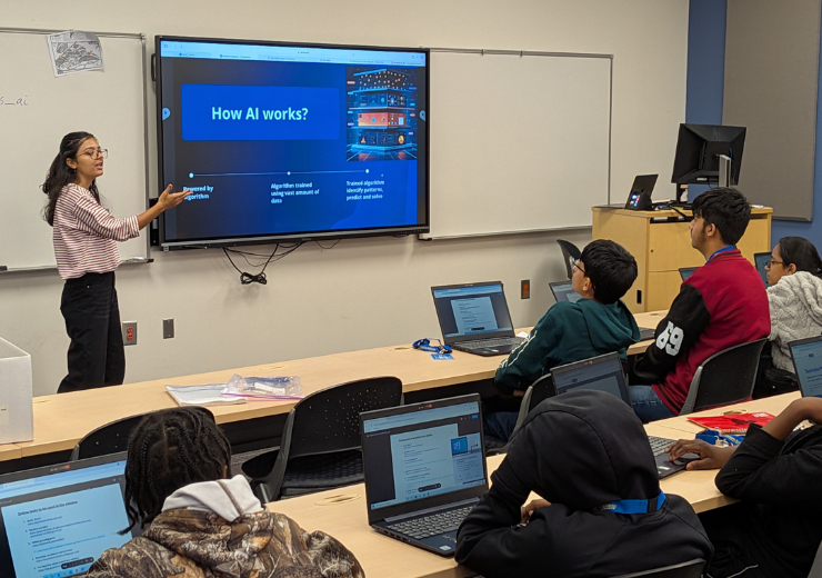 Kusum Neupane presents a slide titled How AI works? to students seated at desks with open laptops in a classroom.