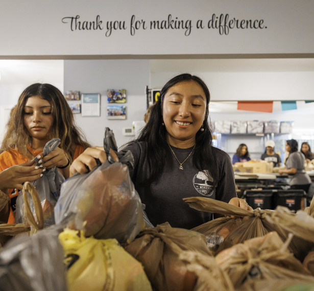 Two Mercer students pack sack lunches into bags at a community center.