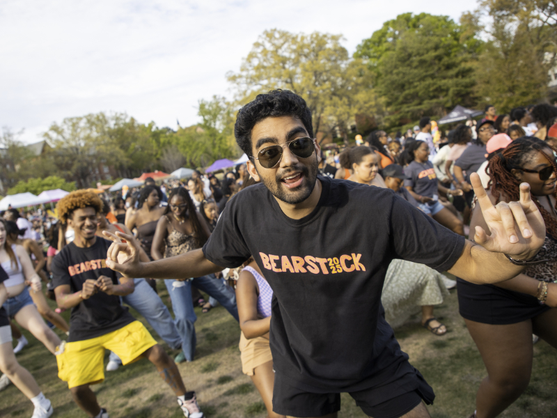 Mercer students dance outdoors at a music festival. The student in front wears sunglasses and a Bearstock shirt.
