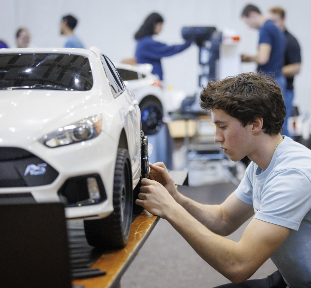 A Mercer student adjusts a wheel on a model car while others work in the background at an indoor event.