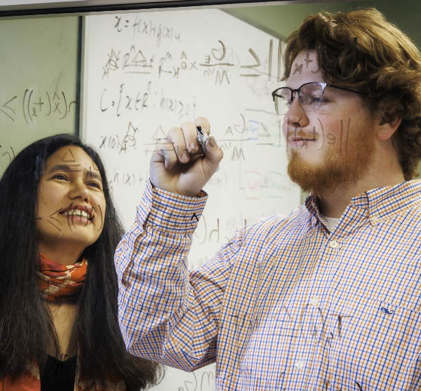 Dr. Makhin Thitsa and Wesley Kinney work at a glass window covered with mathematical equations. Kinney is writing while Dr. Thitsa observes.