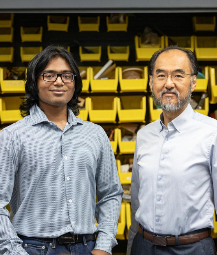 Two men standing in front of shelves with yellow storage bins filled with various items, both looking at the camera.