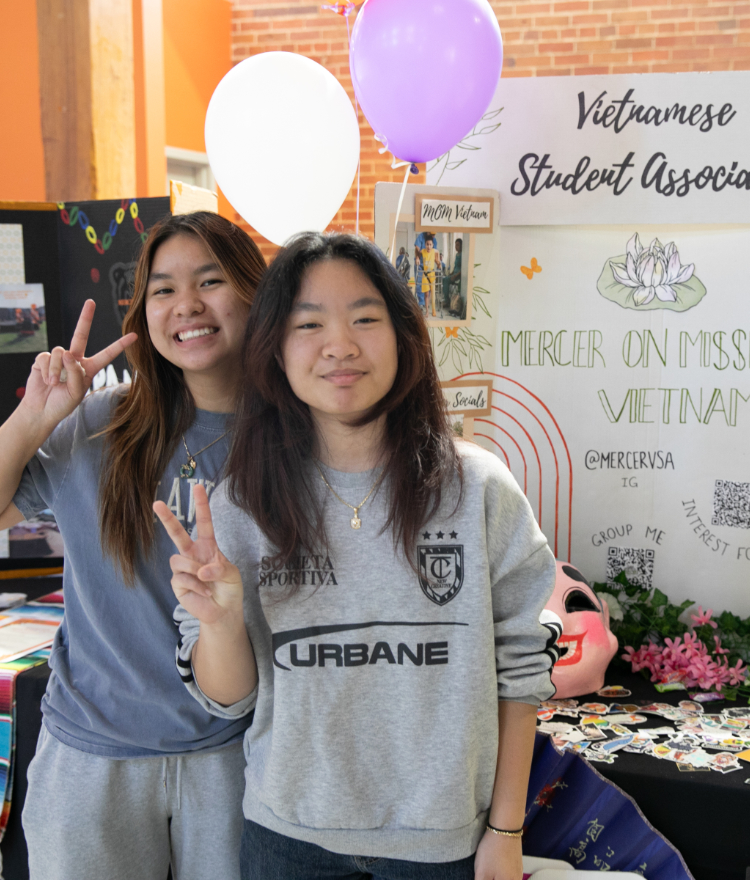 Two Mercer students give peace signs in front of a trifold board for the Vietnamese Student Association.