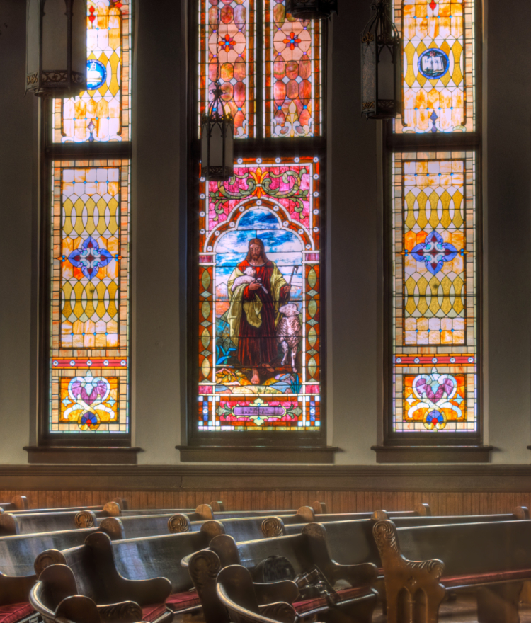 Interior of Mercer University's Newton Chapel with wooden pews and large stained glass windows featuring Jesus.