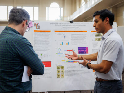 A Mercer student explains his research poster about gene regulation to a man.